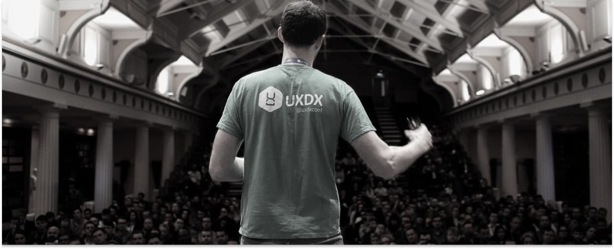 A speaker on stage at a UXDX event speaking to a large audience